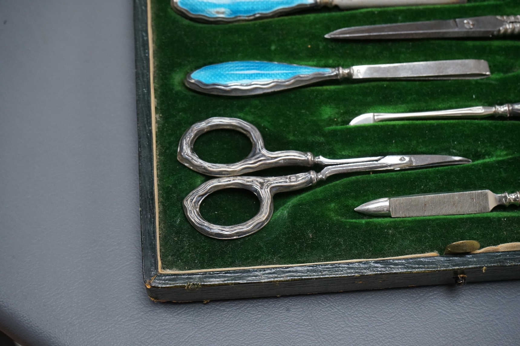 A cased George V eight piece (ex 9 piece) manicure and toilet jar set, comprising seven silver and enamel mounted items, Boots Pure Drug Company, Chester and Birmingham, 1910, together with a matching pair of steel sciss